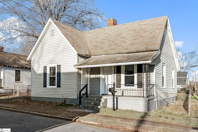 view of front of house featuring a porch, a chimney, and a shingled roof