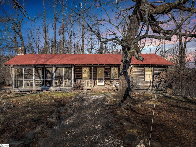 view of front of home with a sunroom, log exterior, and a chimney