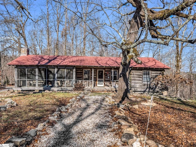 view of front of home featuring a sunroom, covered porch, driveway, and a chimney