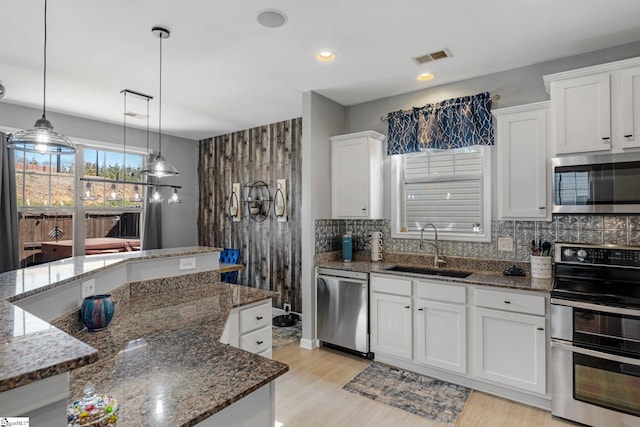 kitchen with backsplash, light wood-style flooring, appliances with stainless steel finishes, white cabinets, and a sink