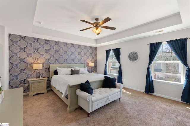 bedroom with a tray ceiling, visible vents, an accent wall, baseboards, and wallpapered walls