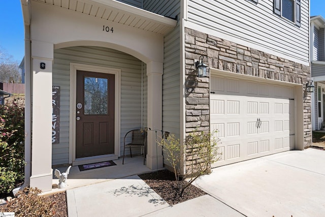 property entrance with a garage, stone siding, and concrete driveway