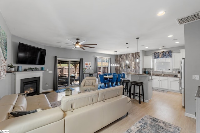 living area with light wood finished floors, a fireplace with flush hearth, and visible vents