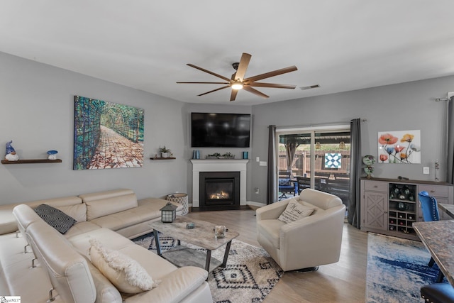 living area featuring a fireplace with flush hearth, visible vents, ceiling fan, and wood finished floors