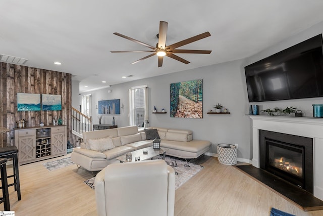 living room with wood finished floors, stairway, a glass covered fireplace, and visible vents