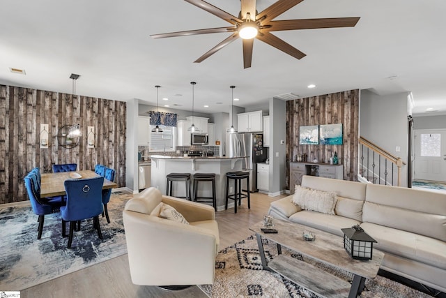 living area featuring an accent wall, light wood finished floors, stairway, and wooden walls