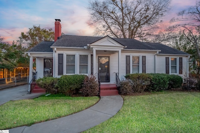 view of front of home featuring roof with shingles, a lawn, a chimney, and fence