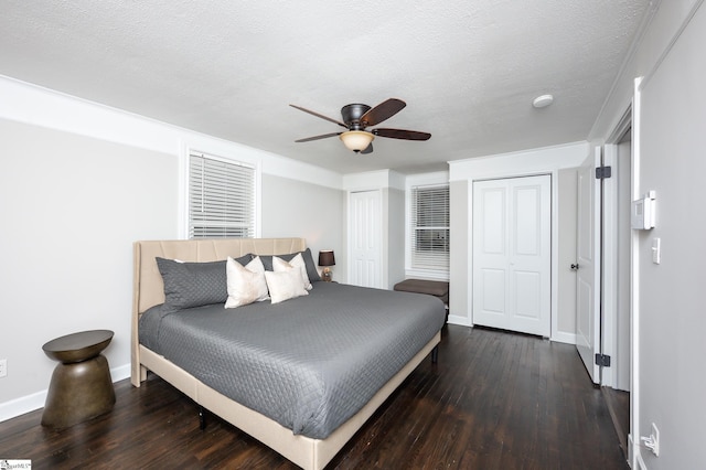 bedroom with baseboards, ceiling fan, wood finished floors, a textured ceiling, and two closets