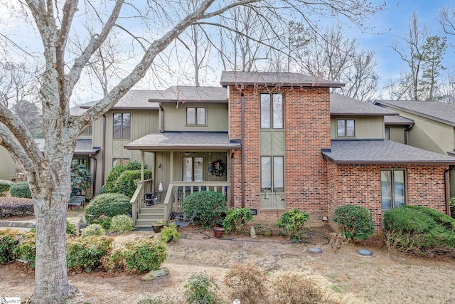 view of front of property featuring covered porch, brick siding, and roof with shingles