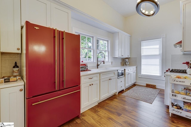 kitchen with high quality fridge, wood finished floors, a sink, white cabinetry, and light countertops