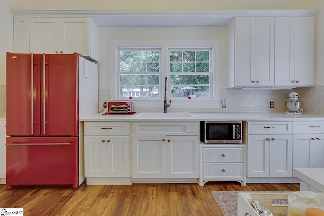 kitchen with a sink, white cabinets, light wood-style floors, high end fridge, and stainless steel microwave