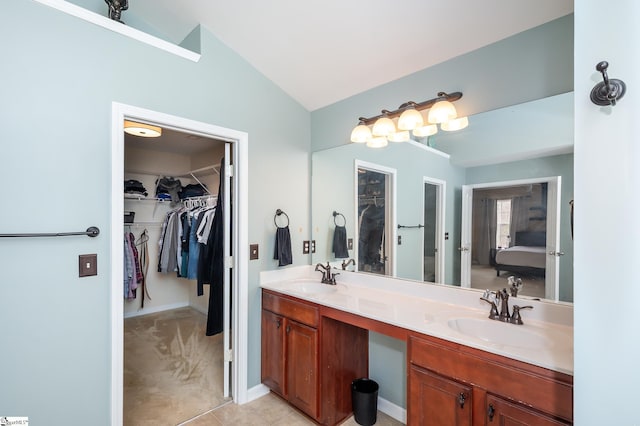 bathroom with vaulted ceiling, double vanity, a sink, and a walk in closet