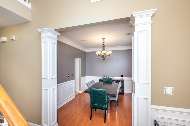 dining space featuring a wainscoted wall, visible vents, wood finished floors, and decorative columns