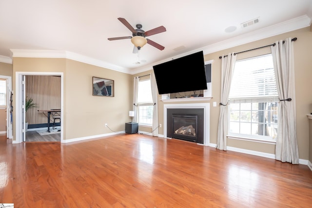 unfurnished living room with baseboards, visible vents, a glass covered fireplace, wood finished floors, and crown molding