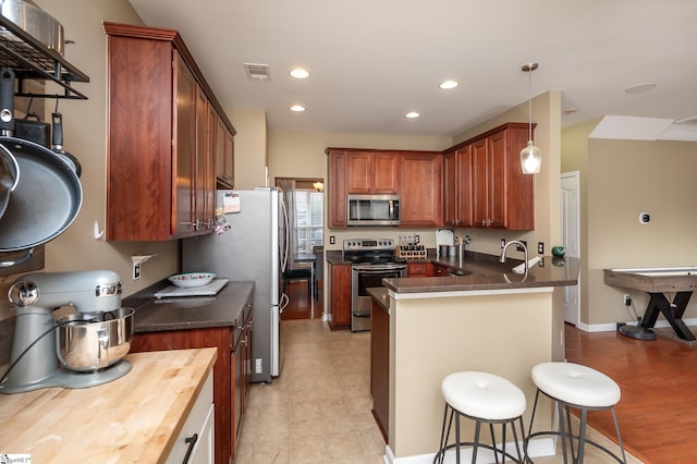 kitchen featuring decorative light fixtures, stainless steel appliances, recessed lighting, a peninsula, and a kitchen bar