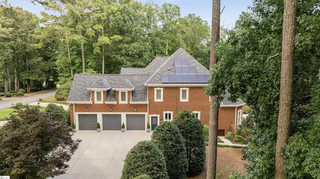 view of front of house with concrete driveway, brick siding, an attached garage, and roof mounted solar panels