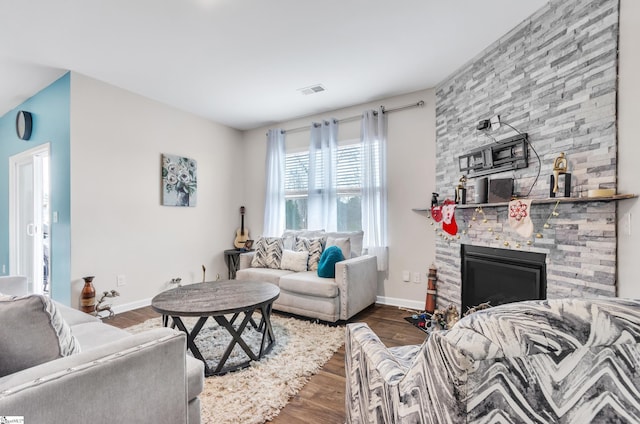 living area featuring dark wood-type flooring, visible vents, a stone fireplace, and baseboards