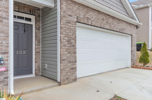 doorway to property featuring a garage, brick siding, and driveway