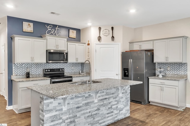 kitchen featuring a center island with sink, light wood-style flooring, appliances with stainless steel finishes, light stone countertops, and a sink