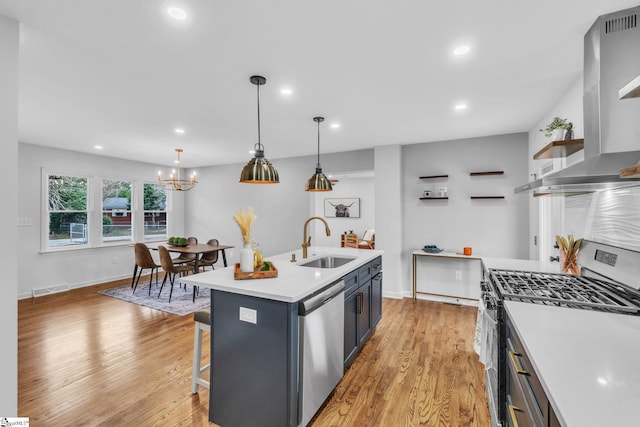 kitchen featuring a sink, light wood-style floors, wall chimney range hood, appliances with stainless steel finishes, and open shelves