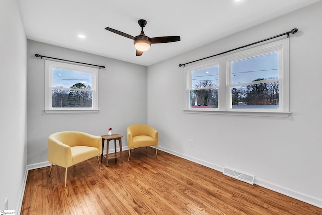 sitting room with light wood-type flooring, visible vents, ceiling fan, and baseboards