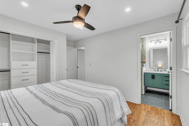 bedroom featuring light wood finished floors, a closet, a ceiling fan, ensuite bath, and baseboards