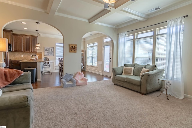 living room featuring arched walkways, coffered ceiling, visible vents, ornamental molding, and beam ceiling