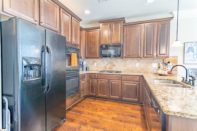 kitchen with light stone counters, dark wood-type flooring, a peninsula, black appliances, and a sink