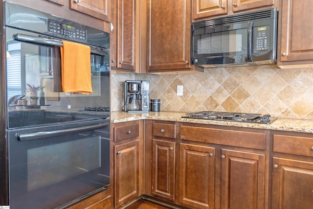 kitchen featuring light stone countertops, black appliances, decorative backsplash, and brown cabinetry