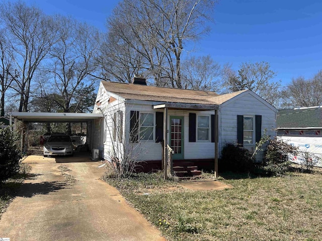 view of front facade featuring driveway, entry steps, a chimney, an attached carport, and a front lawn