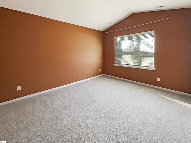 empty room featuring carpet flooring, visible vents, vaulted ceiling, and baseboards