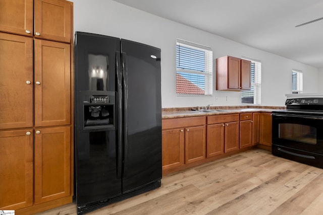 kitchen featuring brown cabinets, black appliances, light wood finished floors, and a sink