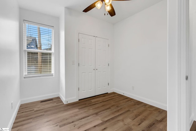 unfurnished bedroom with a closet, visible vents, ceiling fan, wood finished floors, and baseboards