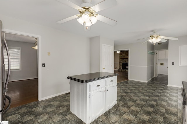 kitchen featuring a fireplace with raised hearth, white cabinetry, baseboards, dark countertops, and stainless steel fridge