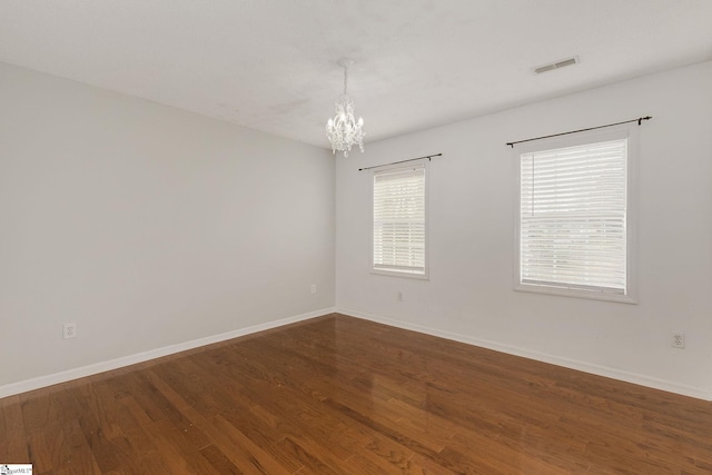 empty room with a notable chandelier, baseboards, visible vents, and dark wood-type flooring