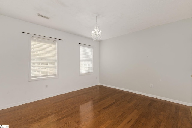 empty room with baseboards, a notable chandelier, visible vents, and wood finished floors