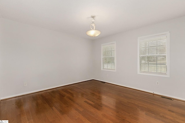 unfurnished room featuring wood finished floors, visible vents, and baseboards