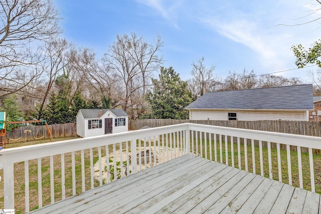 wooden terrace featuring a yard, a fenced backyard, a playground, and an outbuilding