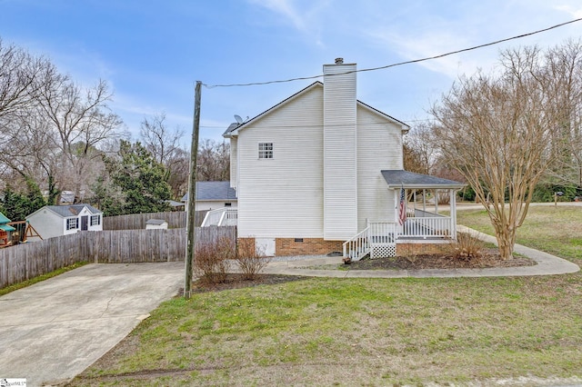 view of side of home with a yard, a chimney, a porch, crawl space, and fence