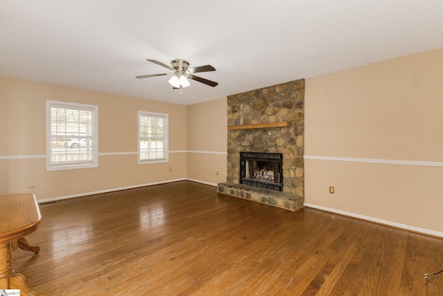 unfurnished living room with a stone fireplace, wood finished floors, a ceiling fan, and baseboards