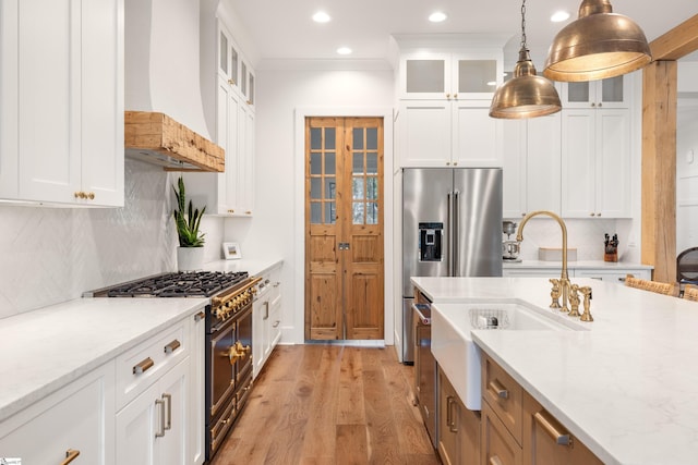 kitchen with decorative light fixtures, light wood finished floors, custom exhaust hood, high end appliances, and tasteful backsplash