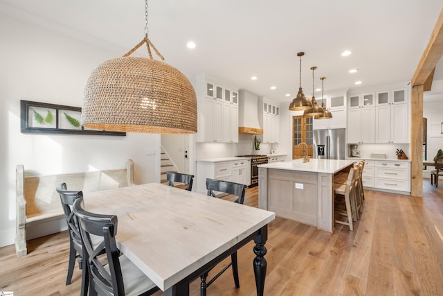 kitchen featuring stainless steel appliances, light countertops, light wood-style floors, wall chimney range hood, and an island with sink