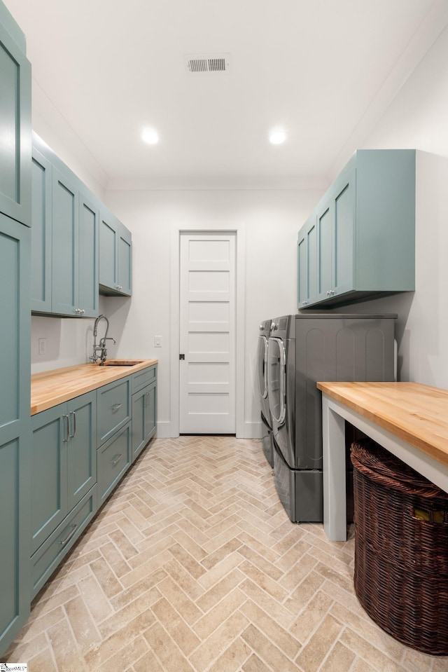 clothes washing area with brick floor, washing machine and clothes dryer, cabinet space, visible vents, and a sink