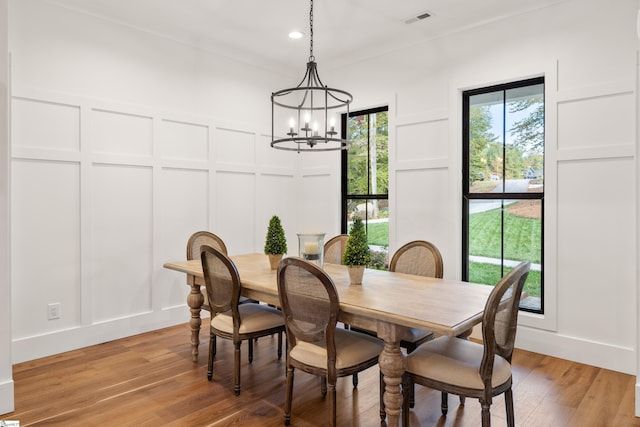 dining space with a notable chandelier, light wood-style floors, visible vents, and a decorative wall