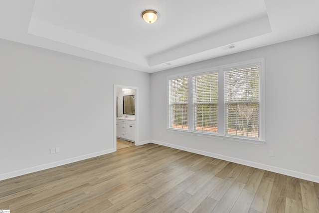 spare room featuring light wood finished floors, baseboards, visible vents, and a raised ceiling