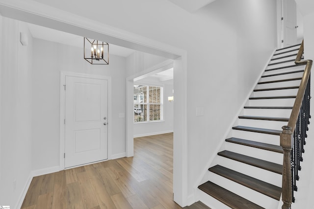 entrance foyer featuring light wood-style flooring, stairs, baseboards, and a notable chandelier