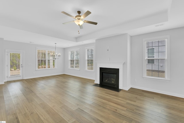 unfurnished living room featuring light wood-type flooring, a raised ceiling, and a healthy amount of sunlight