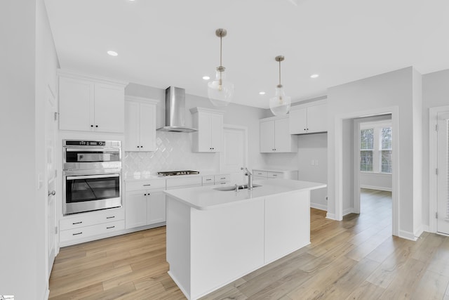 kitchen featuring stainless steel double oven, a sink, decorative backsplash, wall chimney exhaust hood, and stovetop