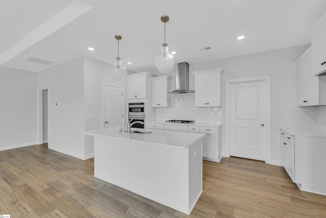 kitchen with tasteful backsplash, visible vents, light wood-style flooring, light countertops, and wall chimney range hood