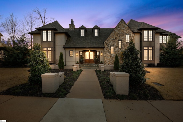 french provincial home with stone siding, french doors, and a chimney